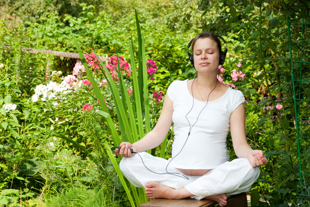 Pregnant Woman with Headphones Relaxing in the Garden